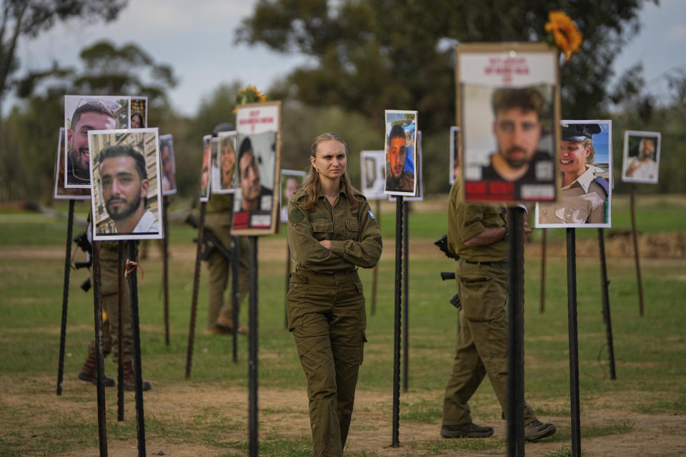 Israeli soldiers look at photos of people killed and taken captive by Hamas militants during their violent rampage through the Nova music festival in southern Israel, which are displayed at the site of the event, as Israeli DJs spun music, to commemorate the October 7, massacre, near Kibbutz Re'im, Tuesday, Nov. 28, 2023. (AP Photo/Ohad Zwigenberg)