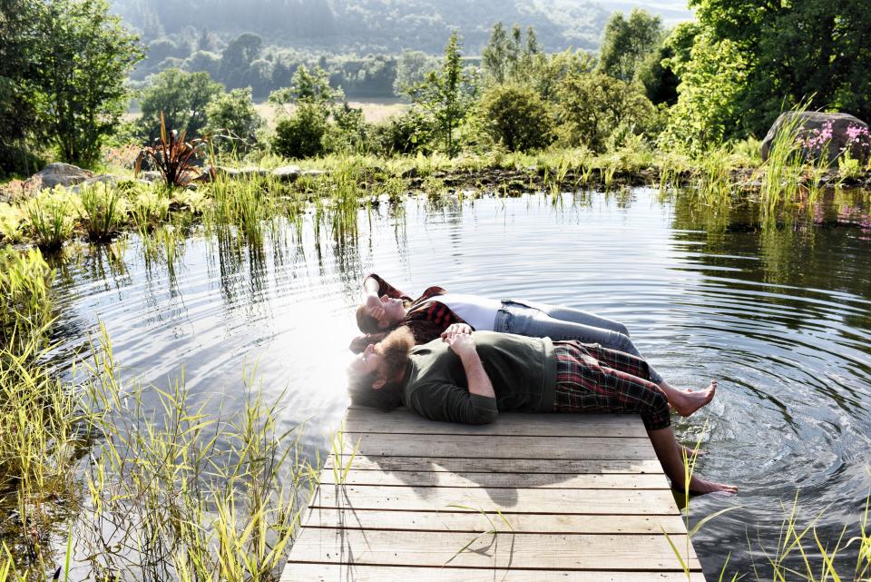 Stef Burgon and her husband Simon Hunt are pictured lying on their backs on the pier of their wild swimming pond.