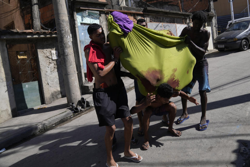 Residents carry a body wrapped in a cloth to a waiting vehicle after a police operation that resulted in multiple deaths in the Complexo do Alemao favela in Rio de Janeiro, Brazil, Thursday, July 21, 2022. Police said in a statement it was targeting a criminal group in Rio's largest complex of favelas, or low-income communities, that stole vehicles, cargo and banks, as well as invaded nearby neighborhoods. (AP Photo/Silvia Izquierdo)