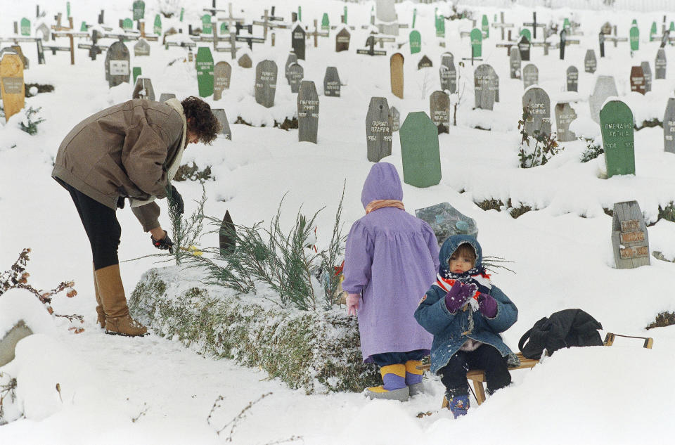 FILE - Fatima Ramic, with her daughter Alma, right and niece Elma, back to camera, tends to the grave of her 8-year-old son, Alija, who died the previous year from medical complications in Sarajevo's Kosevo hospital on Jan. 5, 1995. The mother says her son is a victim of the war due to inadequate facilities and medicines available to the sick and injured of the Bosnian capital. (AP Photo/Rikard Larma, File)