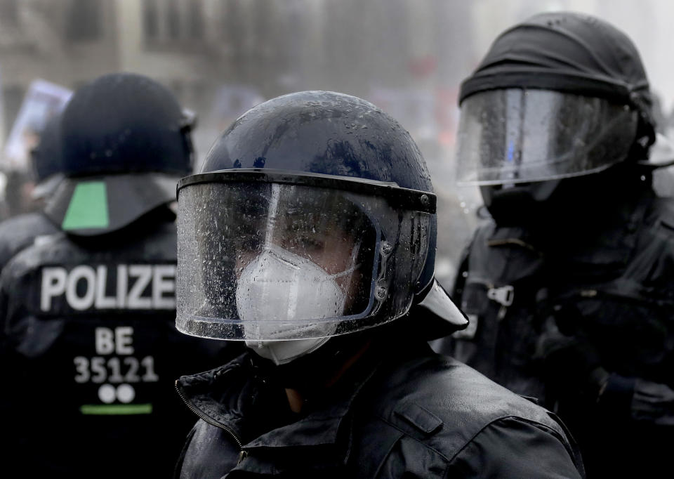 A police person wears a face mask under a helmet after beeing hit by a water canon during a violent protest ralley in a road between the Brandenburg Gate and the Reichstag building, home of the German federal parliament, in Berlin, Germany, Wednesday, Nov. 18, 2020 against the coronavirus restrictions in Germany. Police in Berlin have requested thousands of reinforcements from other parts of Germany to cope with planned protests by people opposed to coronavirus restrictions. (AP Photo/Michael Sohn)