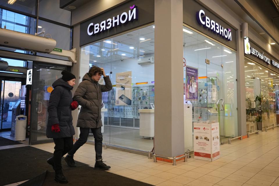 People walk past a Sviaznoy mobile phone shop in a shopping mall in St. Petersburg, Russia, Friday, March 10, 2023. Apple has stopped selling products in Russia, but Wildberries, the country's biggest online retailer, offers the iPhone 14 for about the same price as in Europe. Online retailer Svaznoy lists Apple AirPods Pro. (AP Photo)