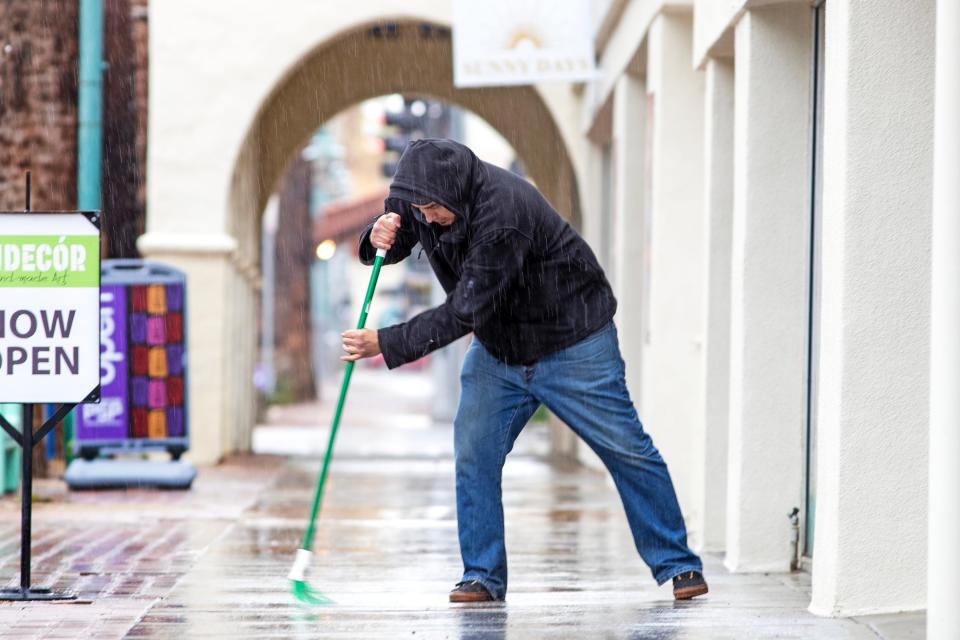 Calvin Cardenas sweeps the sidewalk outside Andecor as rain falls in Palm Springs, Calif., on March 1, 2023.