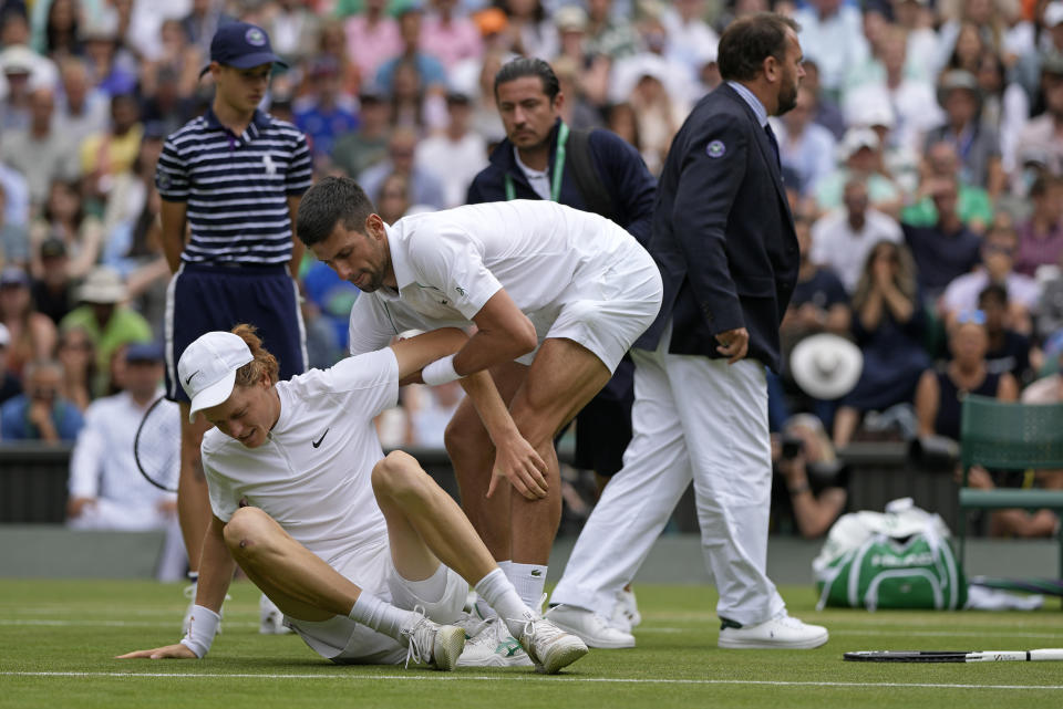 Novak Djokovic auxilia a Jannik Sinner durante el partido por los cuartos de final de Wimbledon, el martes 5 de julio de 2022. (AP Photo/Alastair Grant)