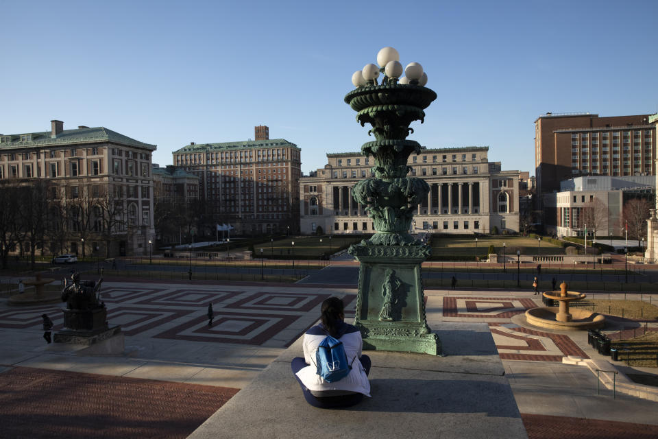 A woman sits on the Columbia University campus, Monday, March 9, 2020, in New York. Colleges nationwide, including Columbia, are shutting down campuses with plans to continue instruction online, leaving some students distressed over where to go and professors puzzling over how to keep up higher education as they know it in the time of coronavirus. Dozens of colleges have canceled in-person classes temporarily or the balance of the semester. (AP Photo/Mark Lennihan)