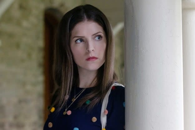 Anna Kendrick looks pensively to the side while standing next to a pillar, wearing a dark top with colorful circular embellishments