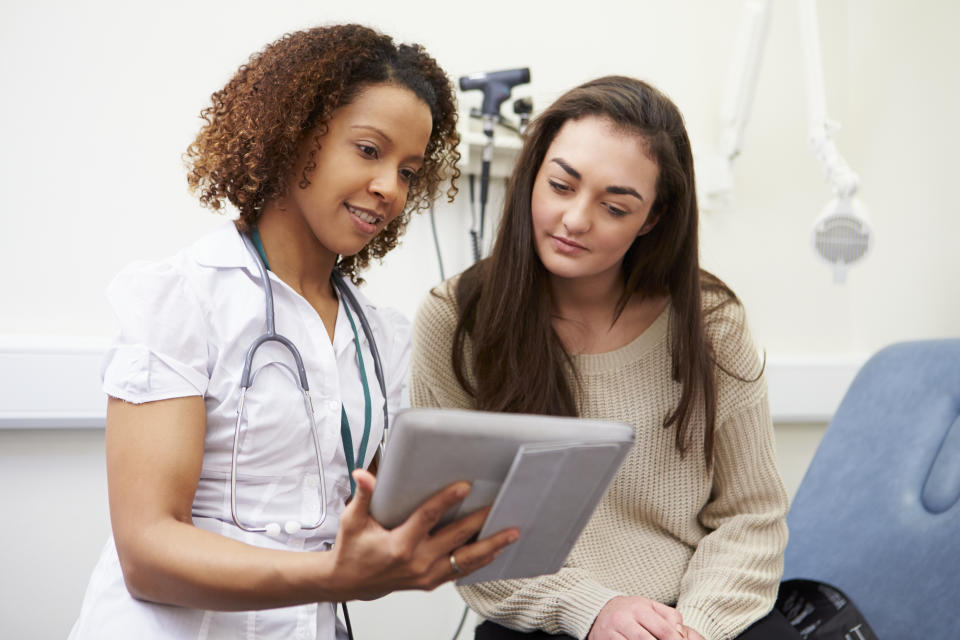 Nurse Showing Patient Test Results On Digital Tablet In Clinic Sitting Down