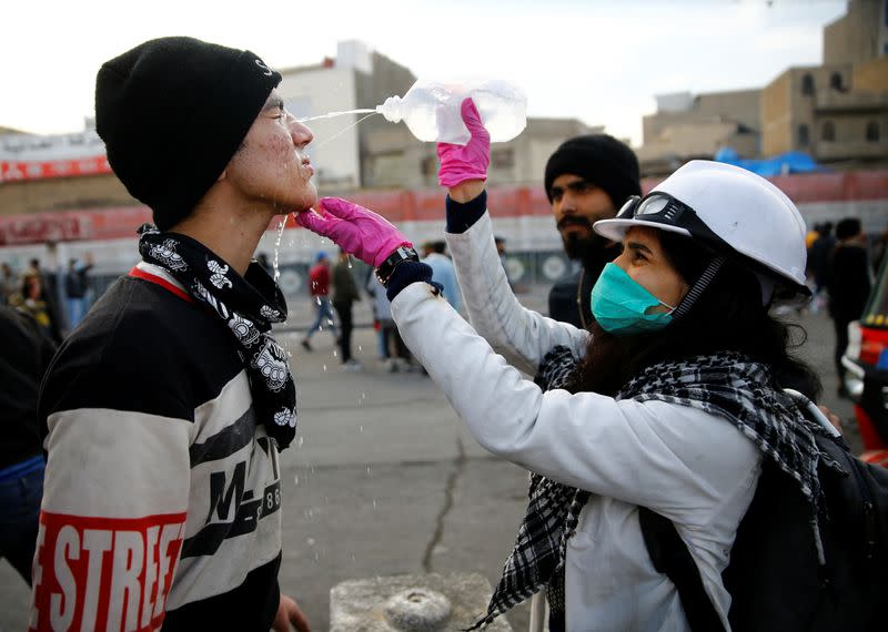 A paramedic woman pours medical fluid on the face of a demonstrator who was affected by tear gas during ongoing anti-government protests in Baghdad