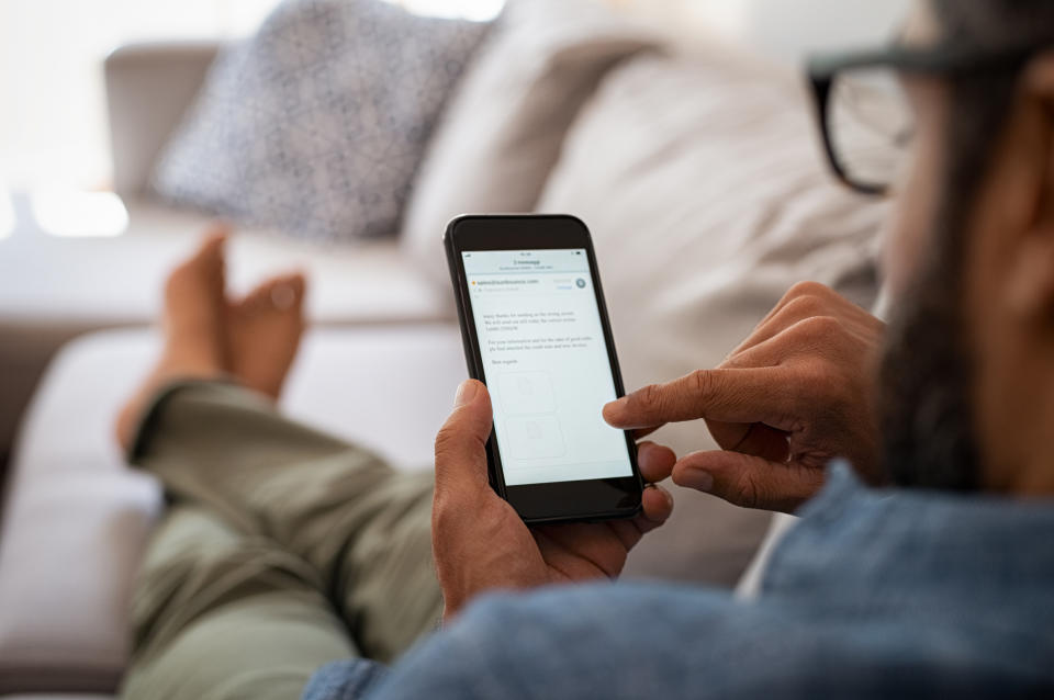 Closeup of a man hand holding cellphone with internet browser on screen. Man with spectacles relaxing sitting on couch while looking at mobile phone. Closeup of mature latin man using smartphone to checking email at home.