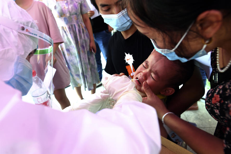 A medical worker takes swab samples from a chid during mass testing for COVID-19 at a residential block in Wuhan in central China's Hubei province Tuesday, Aug. 3, 2021. China suspended flights and trains, canceled professional basketball league games and announced mass coronavirus testing in Wuhan on Tuesday as widening outbreaks of the delta variant reached the city where the disease was first detected in late 2019. (Chinatopix via AP)