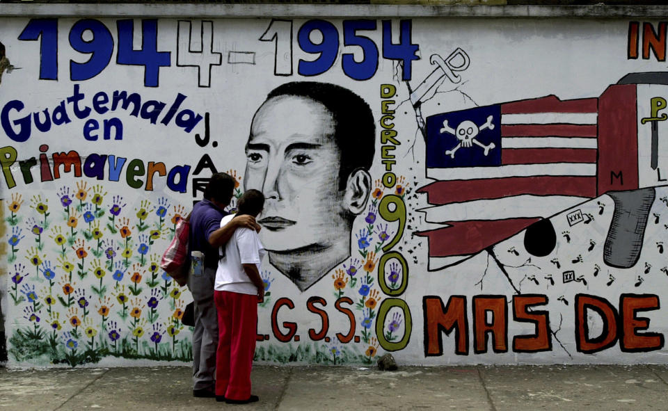 ARCHIVO - En esta fotografía del 16 de junio de 2004 una pareja camina frente a un mural en el centro de Guatemala, en el 50mo aniversario de la intervención militar apoyada por la CIA en 1954 que derrocó al presidente de izquierda Jacobo Árbenz en Guatemala. (AP Foto/Rodrigo Abd, Archivo)