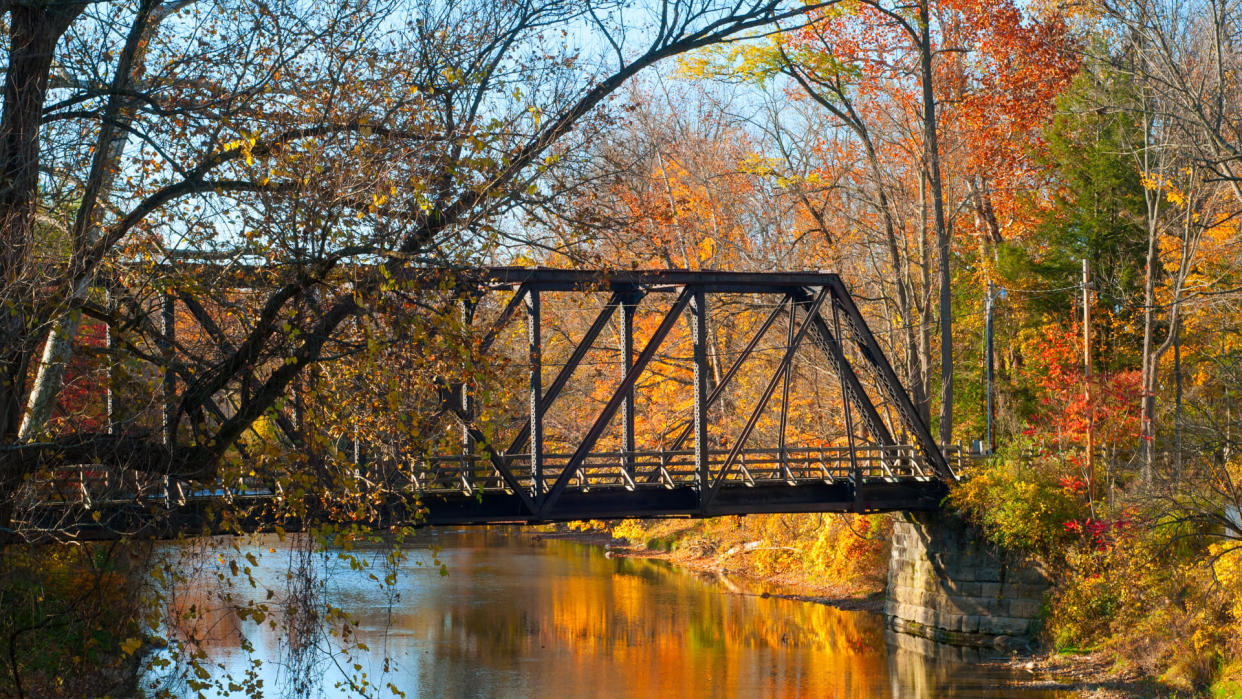 An old pedestrian bridge over an autumn-hued stream - Image.