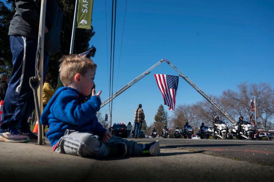 Two-year-old Micah Silva watches a procession go under a large American flag on Elk Grove Boulevard for fallen Elk Grove police officer Tyler Lenehan on Tuesday, Jan. 25, 2022. Lenehan died after he collided with a wrong way driver on his way to work early Friday morning in Sacramento on Jan. 21.