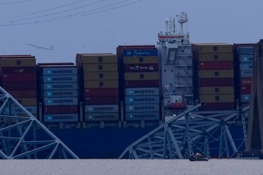 A plane gains altitude as a container ship rests against wreckage of the Francis Scott Key Bridge as night falls on Tuesday, March 26, 2024, as seen from Sparrows Point, Md. The ship rammed into the major bridge in Baltimore early Tuesday, causing it to collapse in a matter of seconds and creating a terrifying scene as several vehicles plunged into the chilly river below. (AP Photo/Matt Rourke)