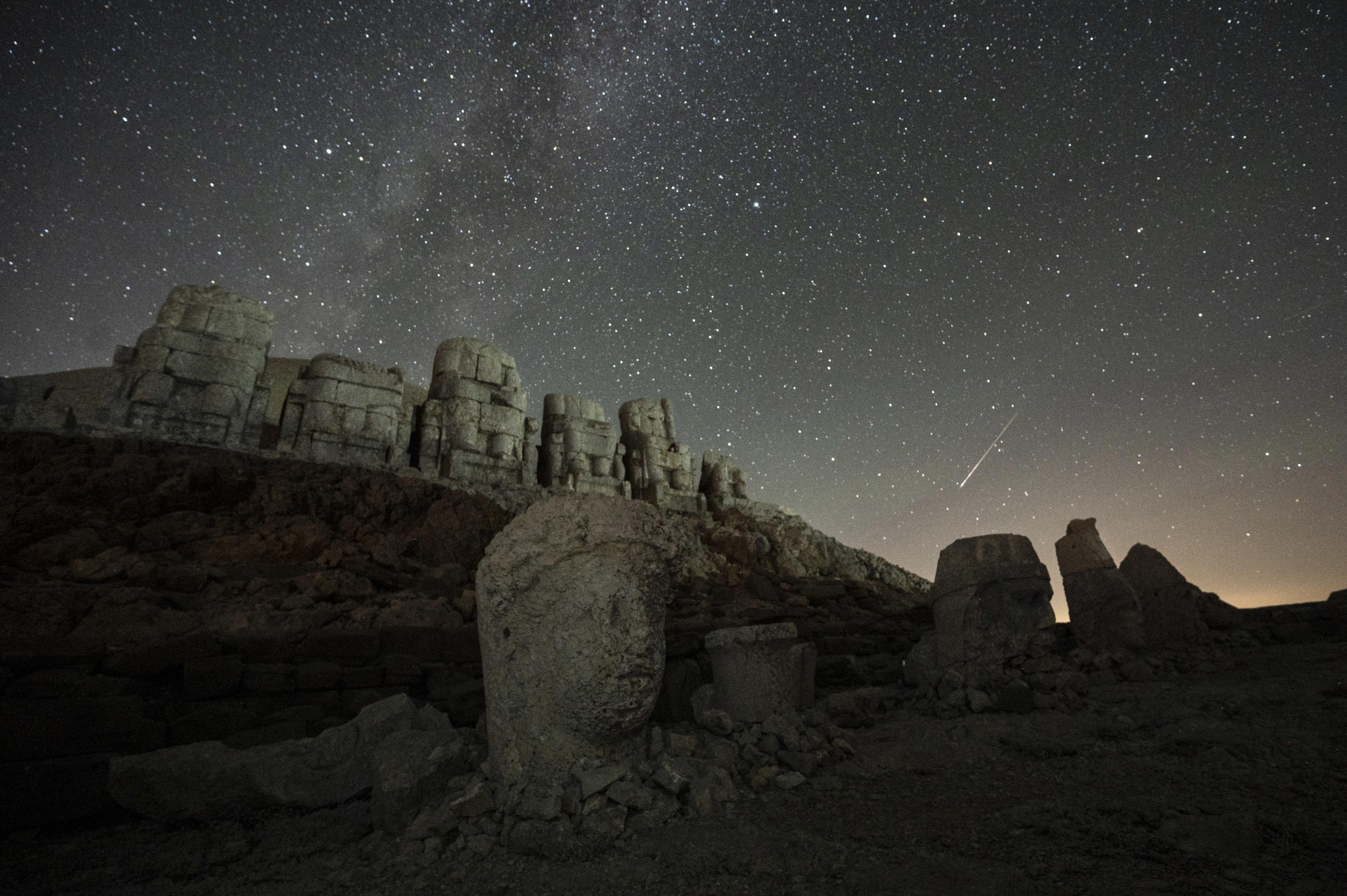 The heads of the massive stone sculptures at the archaeological site of Mount Nemrut can be seen as meteors streaking through the night sky.