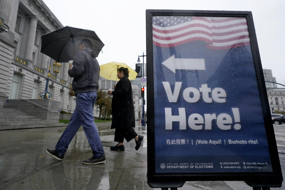 People carry umbrellas while walking past a voting sign outside City Hall in San Francisco, Tuesday, Nov. 8, 2022. A major winter storm pounded California on Tuesday, bringing rain and snow to the drought-stricken state along with possible flash flooding in areas recently scarred by wildfires, meteorologists said. (AP Photo/Jeff Chiu)