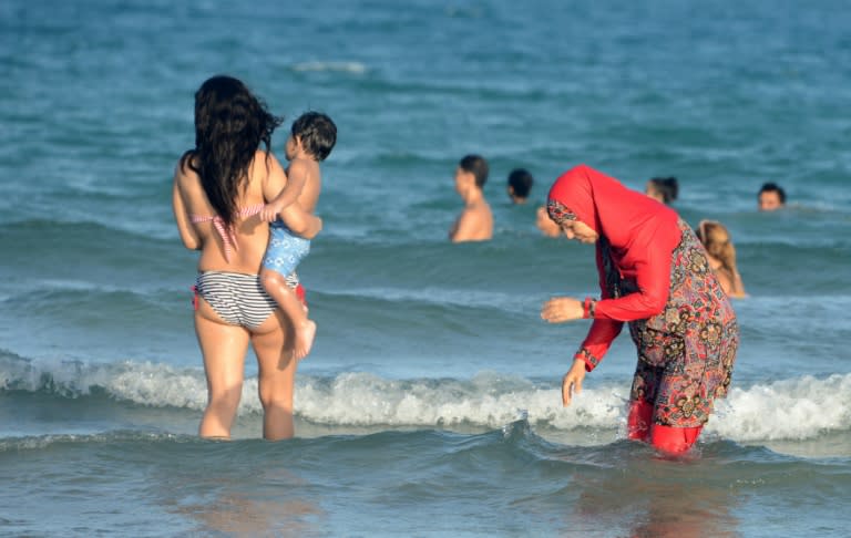 Tunisian women, one wearing a "burkini", walk in the water on August 16, 2016 at Ghar El Melh beach near Bizerte, north-east of Tunis