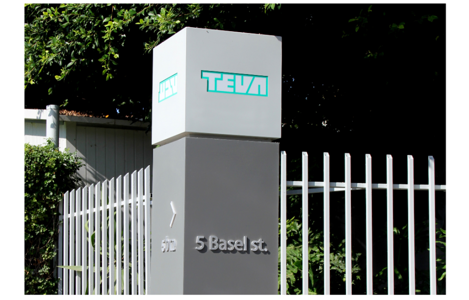 Sign with Teva logo and address, next to a fence and vegetation