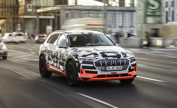 The Audi e-tron quattro prototype, an electric SUV wrapped in black and white camouflage, on a public road in Berlin, Germany.