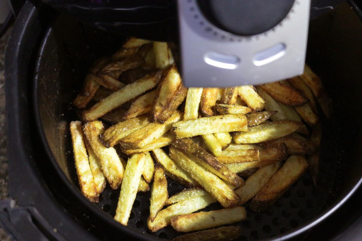 Stock photo showing the inside of an air fryer with a pile of golden brown, freshly cooked French fries / chunky chips. Healthy cooking concept.