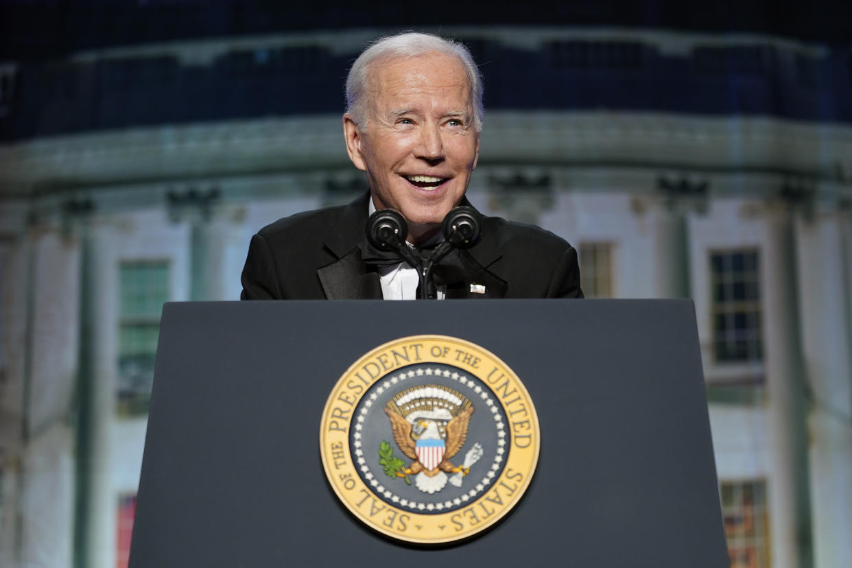 President Biden smiles while standing behind a lectern with the presidential seal on it.