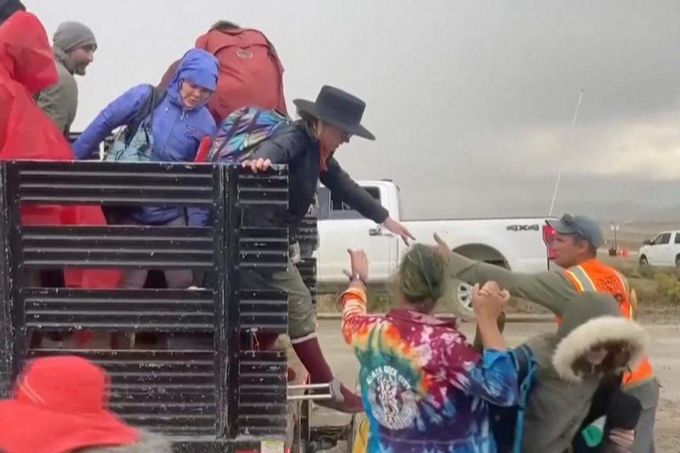 In this image from video provided by Rebecca Barger, festival goers are helped off a truck from the Burning Man festival site in Black Rock, Nev., on Monday, Sept. 4, 2023.