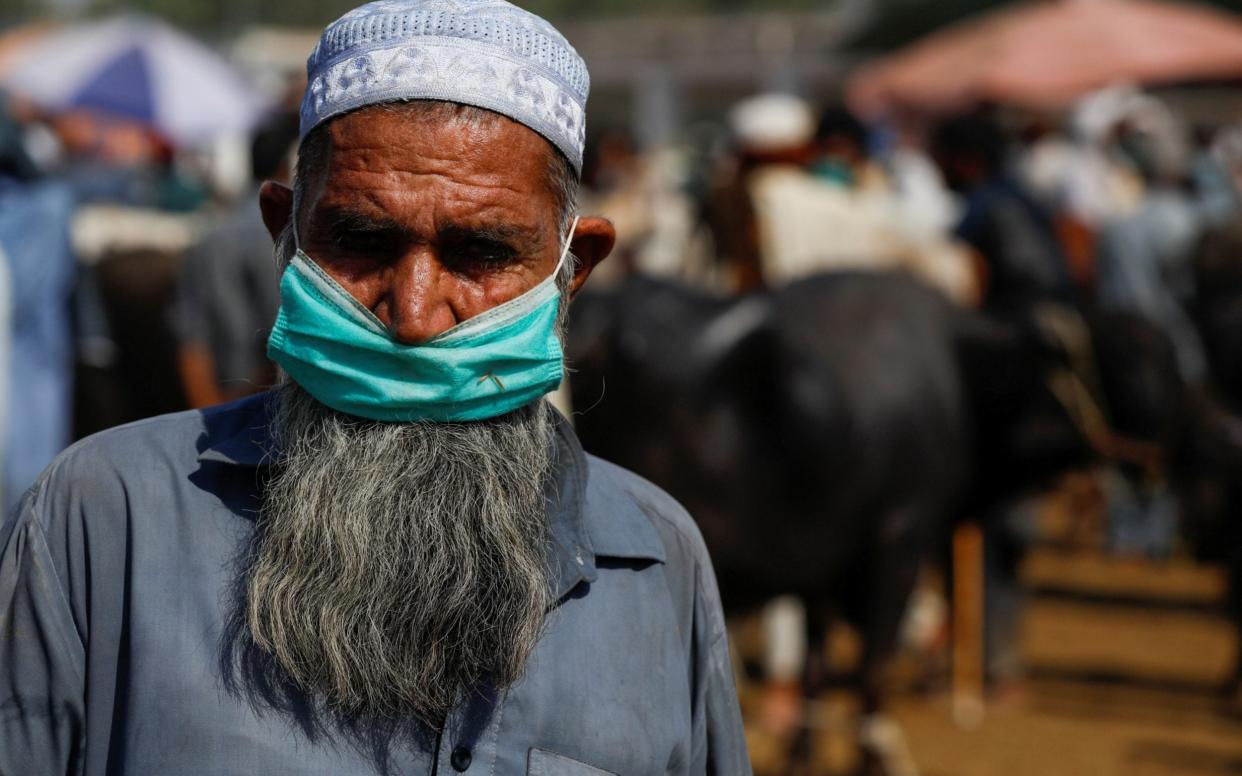 A man wears a protective mask as he sells cows  at the cattle market in Peshaw - REUTERS