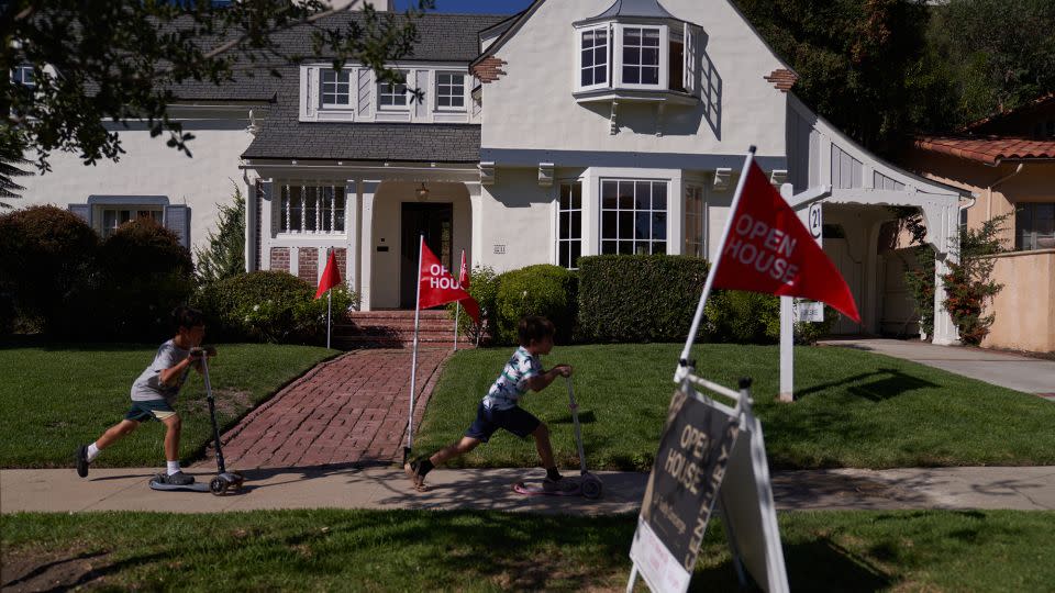 Children ride scooters past and 'open house' flags displayed outside a single family home on September 22, 2022 in Los Angeles, California. - Allison Dinner/Getty Images North America/Getty Images