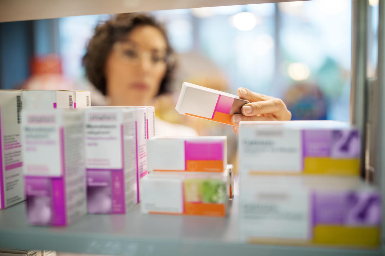 Female pharmacist checking medicines on rack. Chemist examining the medicines at drugstore. Focus on medicine boxes on the shelf.