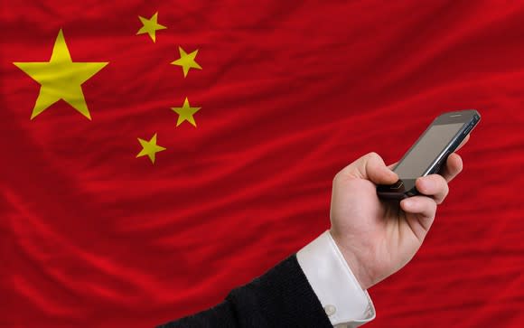 Hand holding mobile device in front of Chinese flag.