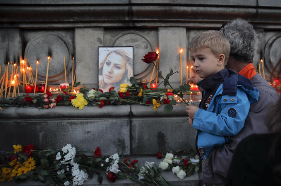 A child holds next to a portrait of slain television reporter Viktoria Marinova during a vigil at the Liberty Monument in Ruse, Bulgaria, Monday, Oct. 8, 2018. Bulgarian police are investigating the rape, beating and slaying of a female television reporter whose body was dumped near the Danube River after she reported on the possible misuse of European Union funds in Bulgaria. (AP Photo/Vadim Ghirda)