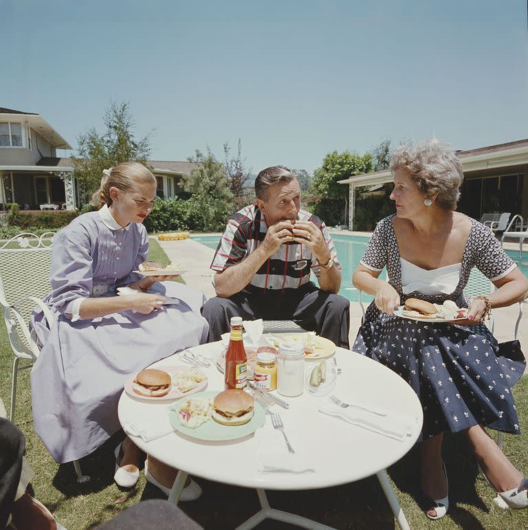 <p>Walt Disney bites into a hamburger while he, his wife Lillian, and their daughter enjoy a poolside lunch in 1955. </p>