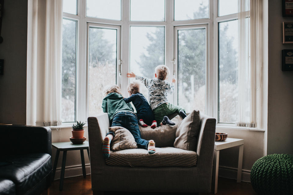 Three children sitting on the back of armchair looking out of a large bay window