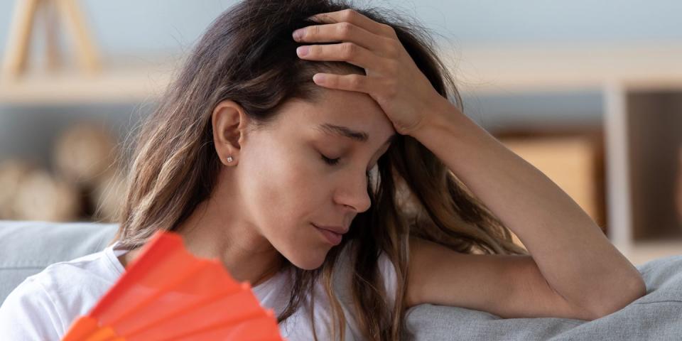 close up woman sitting on couch reducing heat using fan