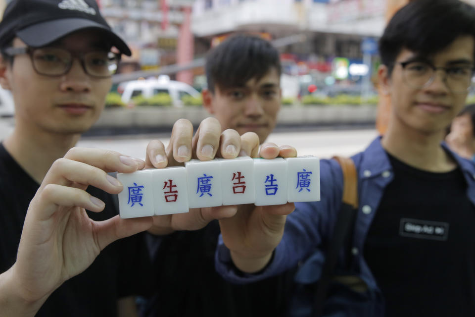 In this April 18, 2019, photo, three students hold their tailor-made mahjong game tiles with Chinese characters engraved by Cheung Shun-king at a shop in Hong Kong. Hand-craved mahjong tiles is a dying art in Hong Kong. But Cheung and mahjong tile shop is trying to revive the heritage/raise people's interest by organizing hand-craved tile class to keep the tradition alive. (AP Photo/Kin Cheung)