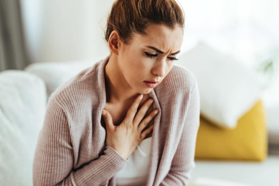 Young woman feeling sick and holding her chest in pain at home.