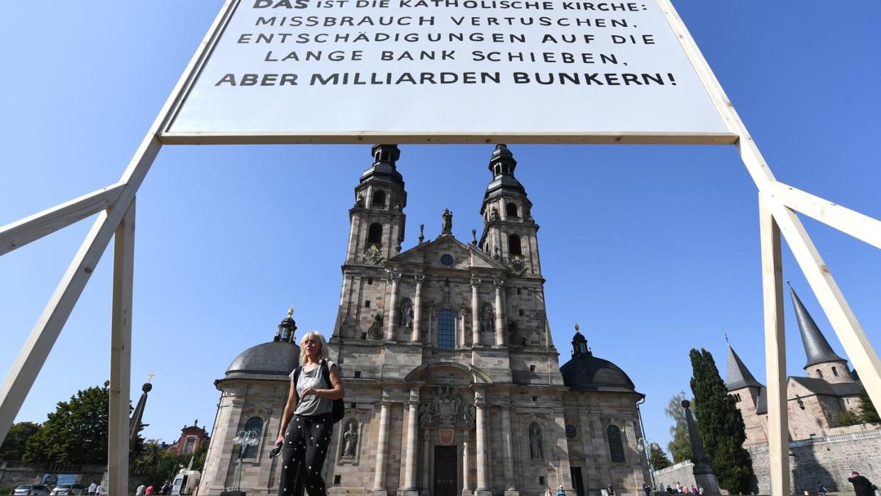 Ein Plakat der Giordano-Bruno-Stiftung mit der Aufschrift "DAS ist die Katholische Kirche: Missbrauch vertuschen. Entschädigungen auf die lange Bank schieben. Aber Milliarden bunkern !" steht am Rande der Herbstvollversammlung der Deutschen Bischofskonferenz auf dem Platz vor dem Dom.