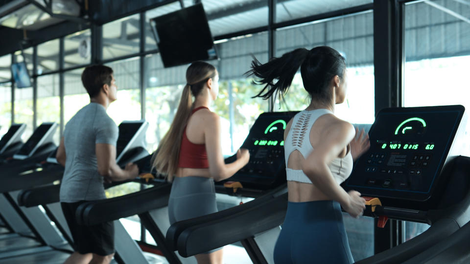 Athletic woman exercising on exercise bike in a gym and talking to his female friend next to him.