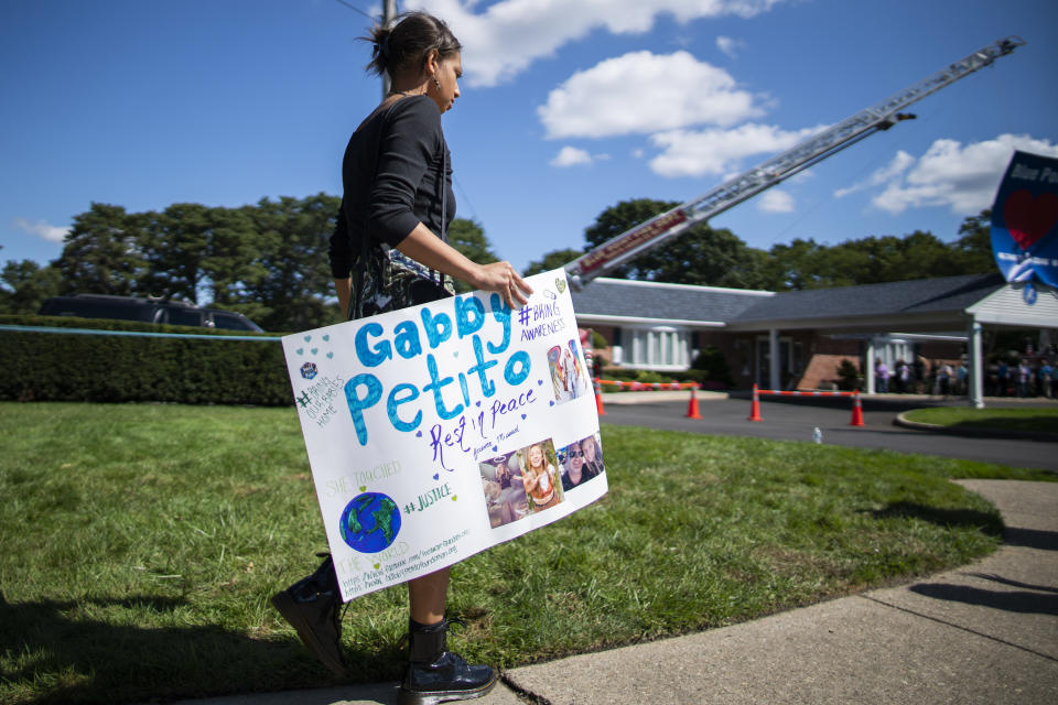 CORRECTS TO FUNERAL HOME VIEWING INSTEAD OF FUNERAL A woman carries a placard in honor of Petito as people attend the funeral home viewing of Gabby Petito at Moloney's Funeral Home in Holbrook, N.Y. Sunday, Sept. 26, 2021. (AP Photo/Eduardo Munoz Alvarez)