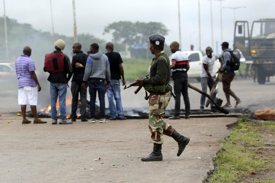 A soldier monitors the removal of a barricade as protestors gather during a demonstration over the hike in fuel prices in Harare, Zimbabwe, Tuesday, Jan. 15, 2019. A Zimbabwean military helicopter on Tuesday fired tear gas at demonstrators blocking a road and burning tires in the capital on a second day of deadly protests after the government more than doubled the price of fuel in the economically shattered country. (AP Photo/Tsvangirayi Mukwazhi)