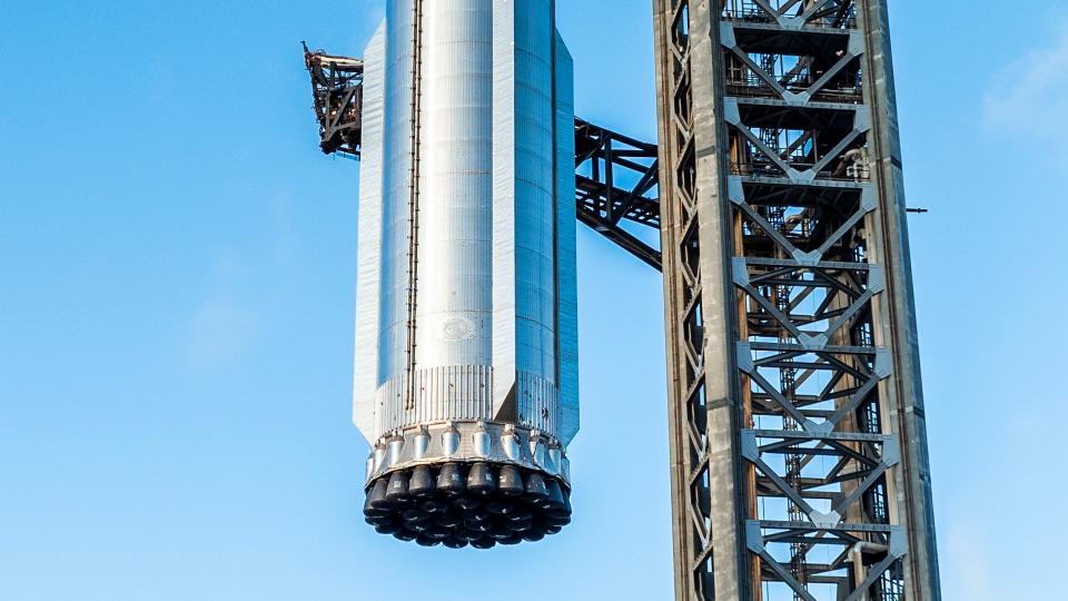 Nahaufnahme der Basis einer riesigen silbernen Rakete, die an einem Startturm hängt und ihre 33 Triebwerke zeigt