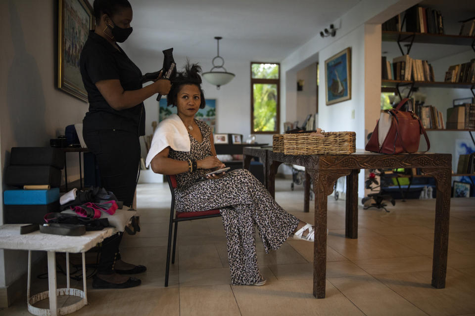 A hairdresser styles the hair of businesswoman Magalie Dresse before she begins a full workday of meetings, in Port-au-Prince, Haiti, Tuesday, Sept. 14, 2021. Since 2004, her car has been attacked; she has survived two kidnapping attempts; the government expropriated some of her properties; and her factory was damaged by arson in riots, costing her $400,000 in a single day. (AP Photo/Rodrigo Abd)