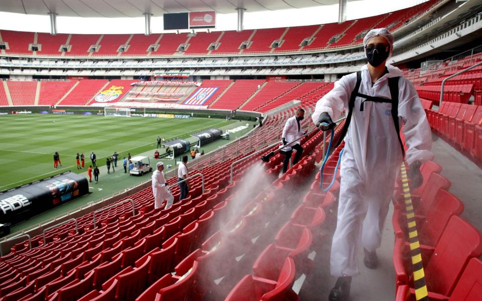 Guadalajara team cleaning staffers disinfect the areas for the football players, before the start of the Mexican football tournament match between Mazatlan and Atlas in Guadalajara, Jalisco state, Mexico - AFP