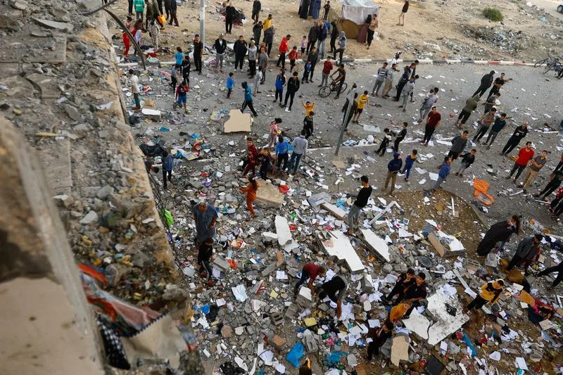 People walk among debris at the site of an Israeli strike on the apartment building, in Khan Younis