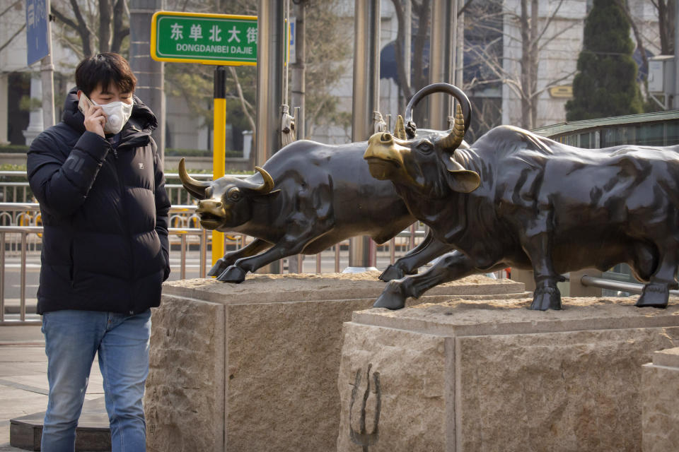 A man wearing a face mask walks past statues of bulls in Beijing, Friday, Feb. 28, 2020. Asian stock markets fell further Friday on spreading virus fears, deepening an global rout after Wall Street endured its biggest one-day drop in nine years. (AP Photo/Mark Schiefelbein)