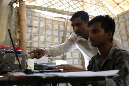 Mohib Bullah, a member of Arakan Rohingya Society for Peace and Human Rights, helps a boy during data entry on a laptop given by Human Rights Watch in Cox's Bazar, Bangladesh, April 21, 2018. Picture taken April 21, 2018. REUTERS/Mohammad Ponir Hossain