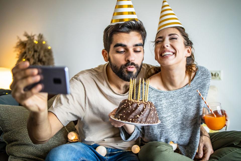 men and woman celebrating birthday at home and young man is blowing birthday candles on the cake