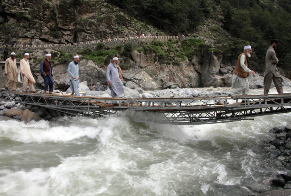 People cross a river on a bridge damaged by floodwaters, in the town of Bahrain, Pakistan, Tuesday, Aug. 30, 2022. The United Nations and Pakistan issued an appeal Tuesday for $160 million in emergency funding to help millions affected by record-breaking floods that have killed more than 1,150 people since mid-June. (AP Photo/Naveed Ali)