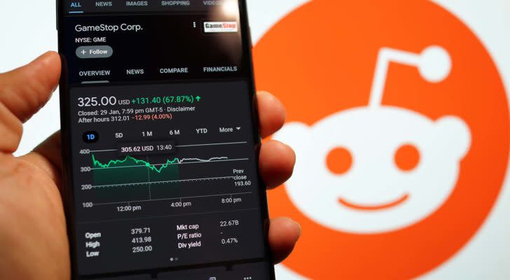 A smartphone shows GameStop (GME) up 70% with the Reddit logo in the background.