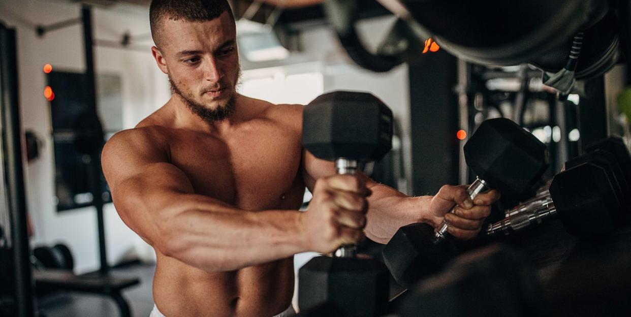 one man, shirtless fit man taking dumbbells from a rack in gym 